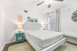 A bedroom with a bed, bedside lamps, a ceiling fan, and a window with curtains.