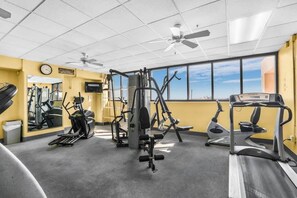 A gym with various exercise equipment, a clock on the wall, and a large window with a city view.