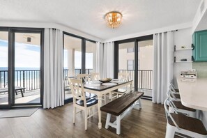 A dining area with a table and chairs, a bench, and a view of the ocean through large windows.
