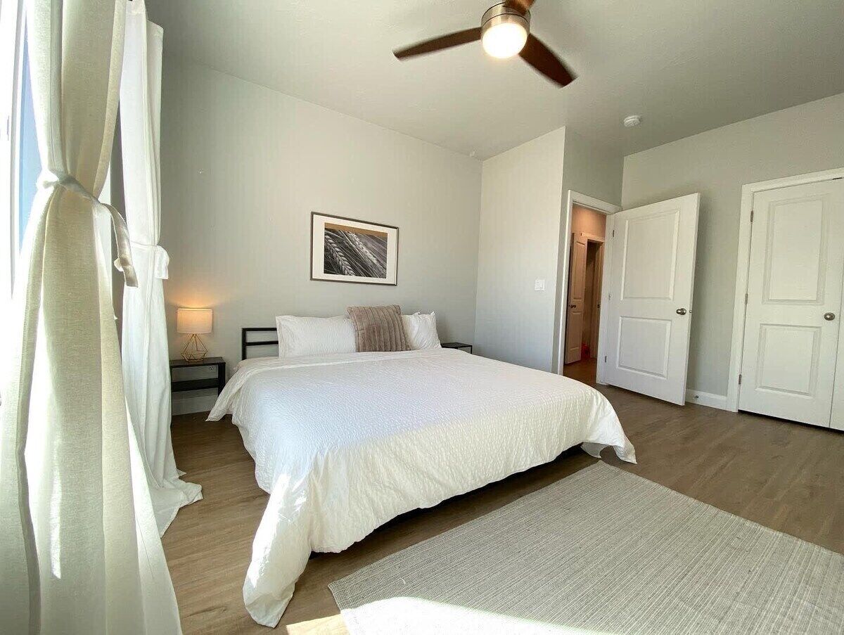 A bedroom with a large bed, a ceiling fan, a bedside lamp, and a framed picture on the wall.