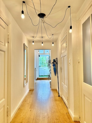 A hallway with wooden flooring, white walls, and a ceiling with hanging light fixtures.