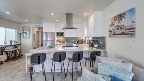 Una cocina moderna con armarios blancos, una isla grande con taburetes de bar y una campana extractora central.