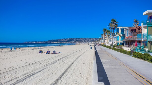 Una playa con cielo despejado, orilla arenosa y edificios a lo largo de la costa.