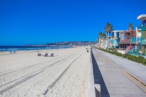 A beach with a clear sky, a sandy shore, and buildings along the coastline.