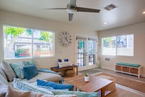 Relax in this spacious living area with a ceiling fan overhead, a large window offering a view of the outside, and a comfortable seating area with a couch and coffee table.
