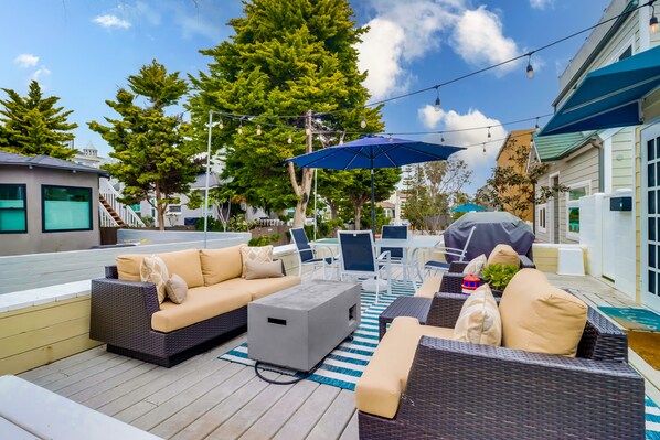 An outdoor patio area with wicker furniture, a gray coffee table, and a blue umbrella.
