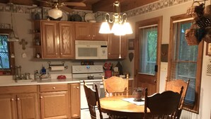 A wooden kitchen with a dining table and chairs, a microwave, and a ceiling fan. - A Hundred Thousand Welcomes! (Newland)