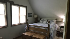 A bedroom with a wooden bed, a bench, a desk, and a window with blinds. - A Hundred Thousand Welcomes! (Newland)