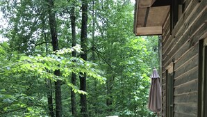 A wooden deck with a railing, two chairs, and a table with an umbrella. - A Hundred Thousand Welcomes! (Newland)