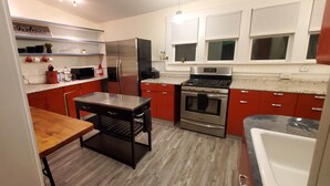 A modern kitchen with red cabinets, stainless steel appliances, and a wooden table. - Great Location Great Value! 4 bedroom 2 full bath home in East Village (Davenport)