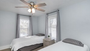 A bedroom with two beds, a ceiling fan, and a nightstand with a lamp. - Great Location Great Value! 4 bedroom 2 full bath home in East Village (Davenport)