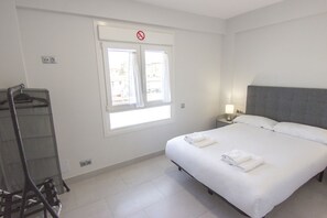 A hotel room with a bed, a nightstand, a lamp, a window with curtains, and a coat rack.