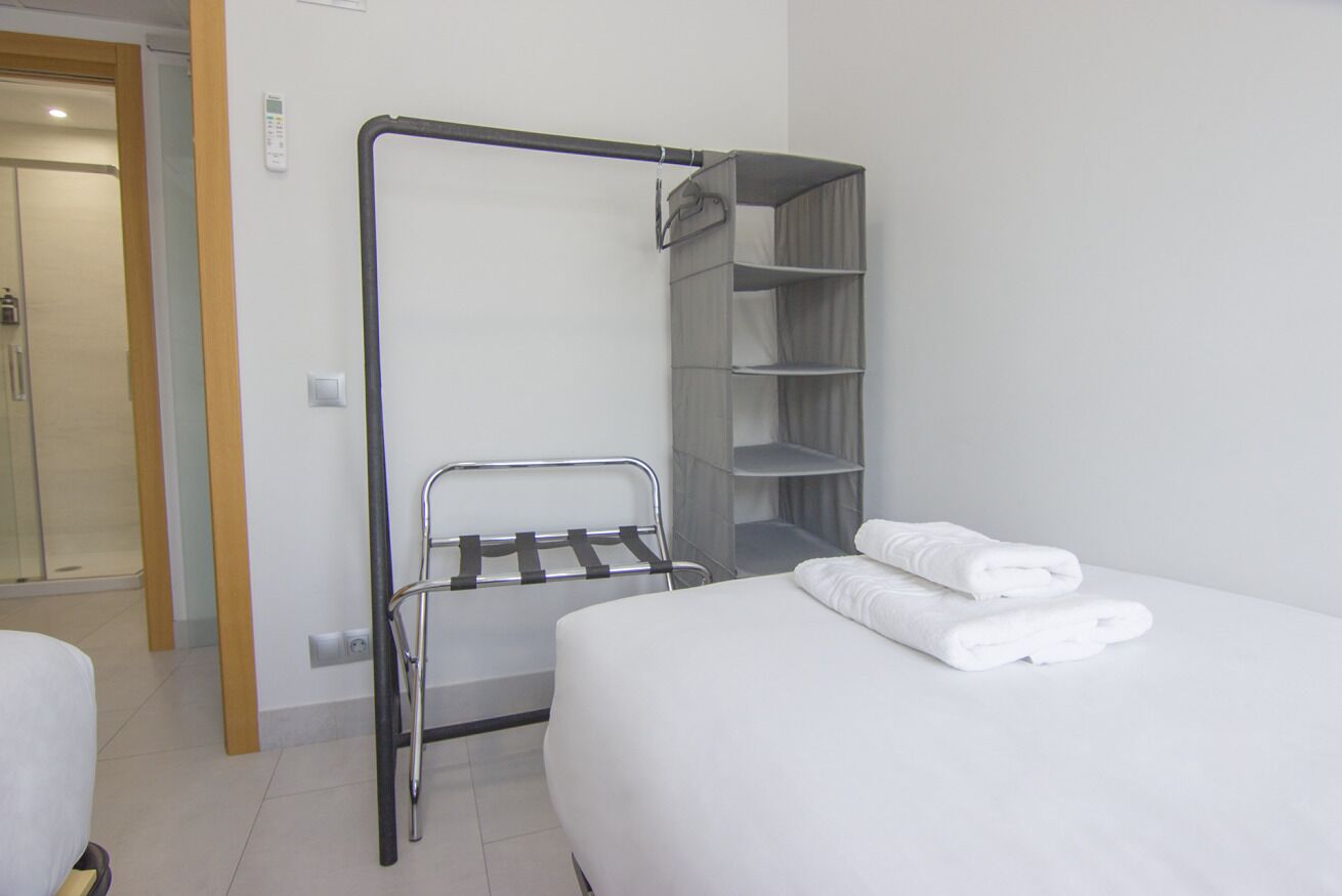 A hotel room with a bed, a towel rack, and a built-in shelf unit.