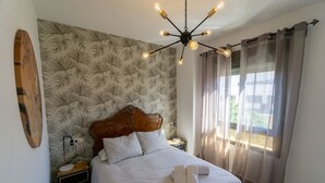 Ein Schlafzimmer mit einem Bett, einem Holz-Kopfteil, einem Nachttisch, einer Lampe, einer Wanduhr und einem Fenster mit Vorhängen.