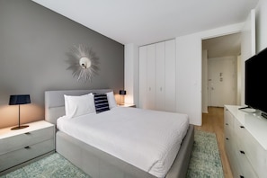 A modern bedroom with a bed, bedside tables, a TV, and a wardrobe.