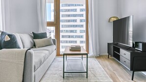 A modern living room with a sofa, a coffee table, a TV, and a view of a building through a glass door. - Amazing Favoriten 3BR w/ Gym & Roof, near Belvedere Palace, by Blueground (Vienna)