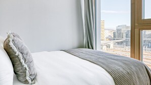 A hotel room with a bed, a view of a cityscape, and a window with curtains. - Amazing Favoriten 3BR w/ Gym & Roof, near Belvedere Palace, by Blueground (Vienna)
