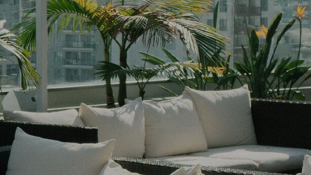 Ein Balkon mit einer Couch, weißen Kissen und Topfpflanzen.