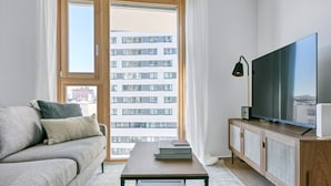 Ein modernes Wohnzimmer mit Sofa, Couchtisch, Fernseher und Blick auf einen Wolkenkratzer.