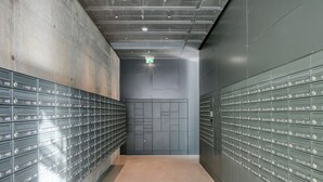 Ein Flur mit Reihen von Metallschließfächern an beiden Seiten, einem Betonboden und einer grauen Wand mit einer Tür am Ende.