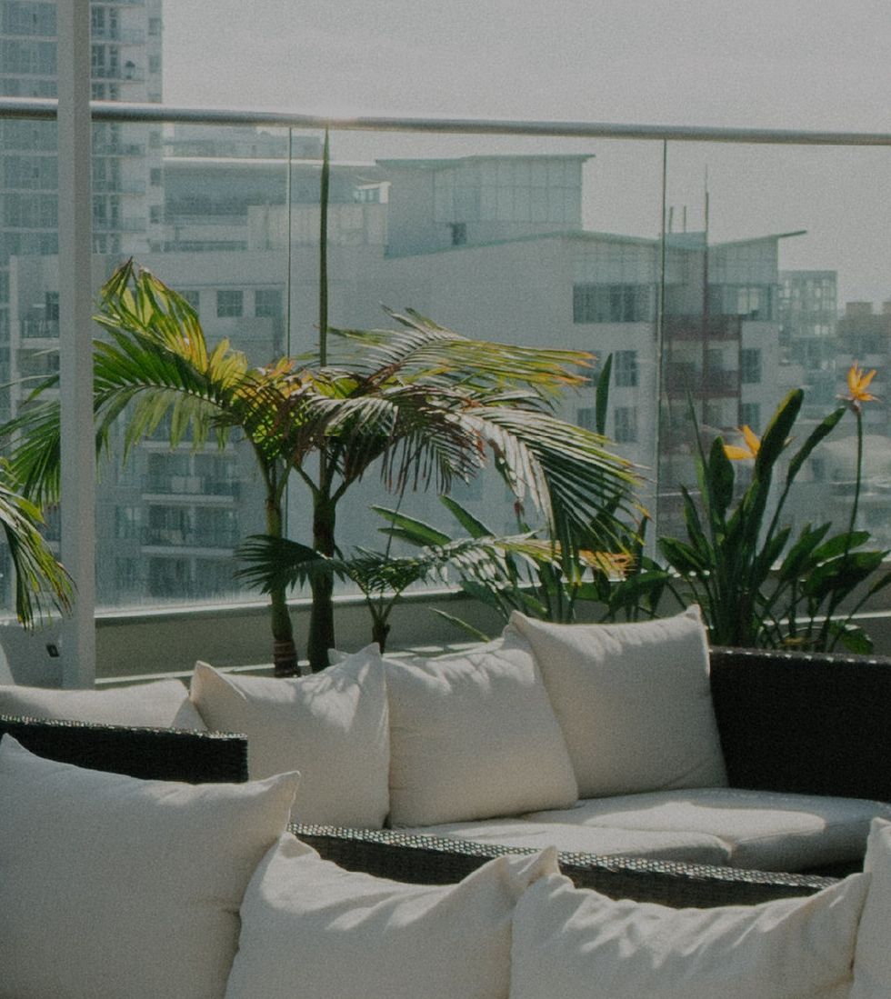 A balcony with a sofa and cushions, potted plants, and a view of buildings.