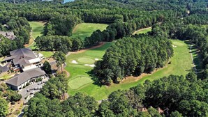 Une vue aérienne d’un terrain de golf entouré de forêts denses, avec un grand bâtiment situé sur le côté gauche.