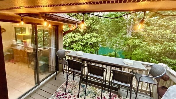 Un balcon avec une table et des chaises, une vue sur les arbres et des guirlandes lumineuses.