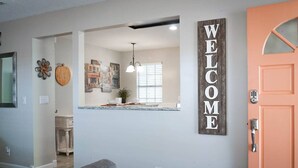 Een moderne keuken met uitzicht op de eetruimte, een 'WELCOME' bord en een deur met een code slot.