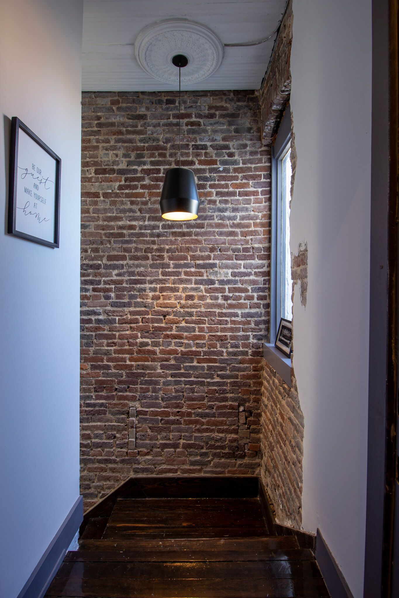Una scala con un muro in mattoni, un lampadario a sospensione e una citazione incorniciata al muro.