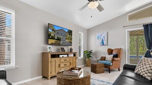 Ein modernes Wohnzimmer mit Fernseher, einer Couch, einem Couchtisch und einem Korbstuhl.