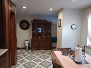 A dining area with a patterned floor, a wooden cabinet, a clock on the wall, and a table with a tablecloth and a roll of paper towels.
