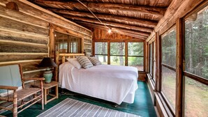 Une chambre située dans une cabane en rondins, avec un lit, une chaise, une lampe et une fenêtre.