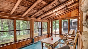 Une cabane avec un intérieur en bois, de grandes fenêtres et une table avec des chaises.