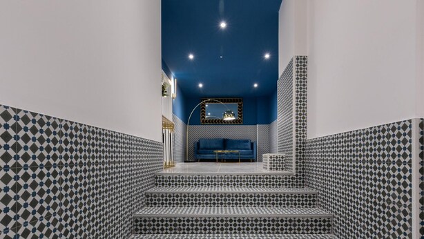 Eine Treppe mit gemusterten Fliesen führt zu einer Sitzgruppe mit einem blauen Sofa und einem kleinen Tisch.