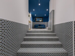 Eine Treppe mit gemusterten Fliesen führt zu einer Sitzgruppe mit einem blauen Sofa und einem kleinen Tisch.