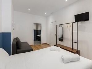 Quarto de hotel moderno com cama, área de estar, espelho e televisão.