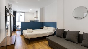 Ein modernes Hotelzimmer mit einem Bett, einer Couch, Holzboden, einem Spiegel und einem Schreibtisch.