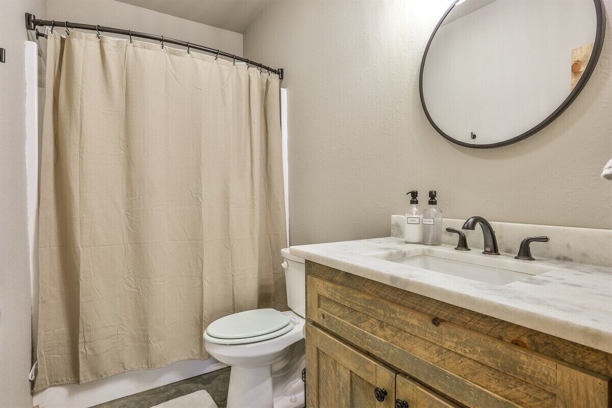 Une salle de bain avec un rideau de douche, des toilettes, un lavabo avec des robinets et un miroir.