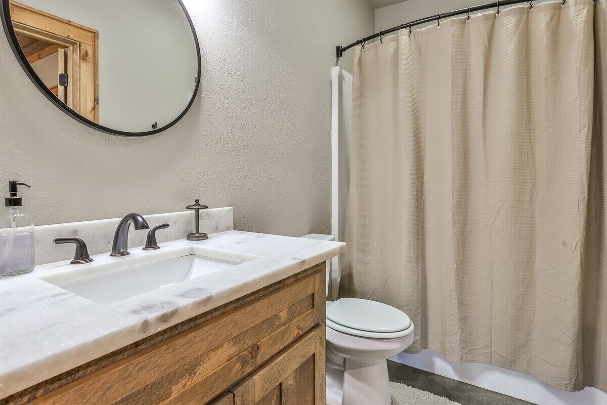 A bathroom with a white sink, two faucets, a mirror, and a toilet.