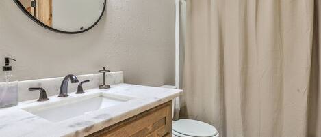 A bathroom with a white sink, two faucets, a mirror, and a toilet.