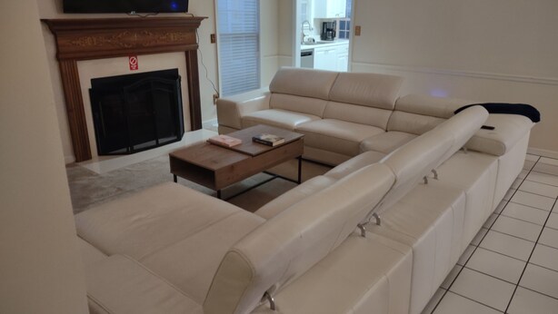 Een woonkamer met een grote beige modulaire bank, een salontafel en een flatscreen televisie die boven een open haard is bevestigd.