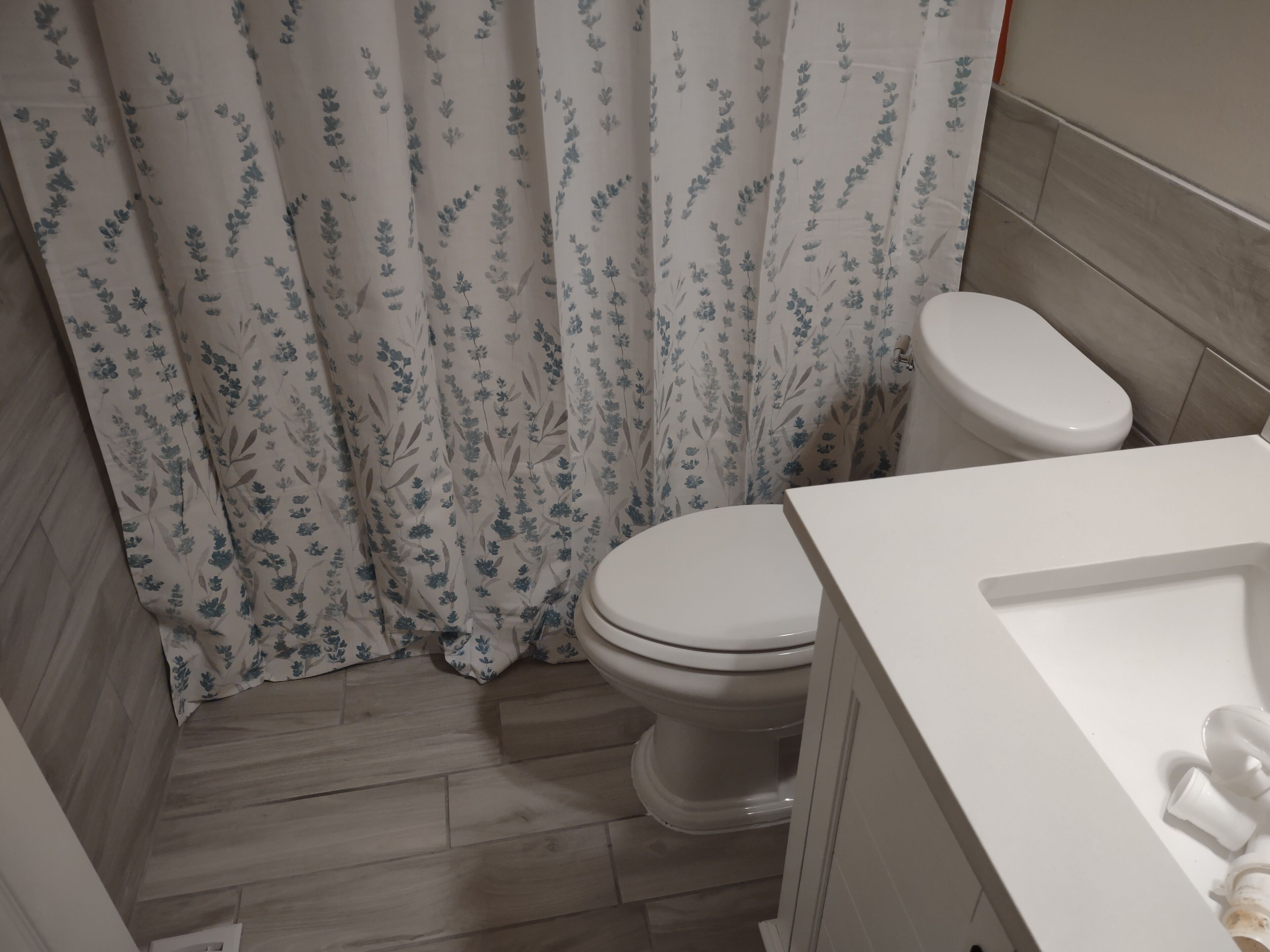 Une salle de bain avec des toilettes, un rideau de douche à motifs floraux et un lavabo blanc.