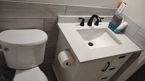Een badkamer met een wit toilet, een wastafel met een zwarte kraan en een blauwe mand met handdoeken.