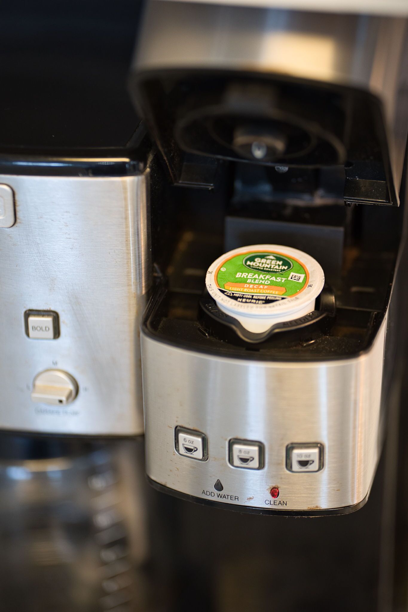 A coffee machine with a coffee pod inserted, a water reservoir, and buttons for operation.