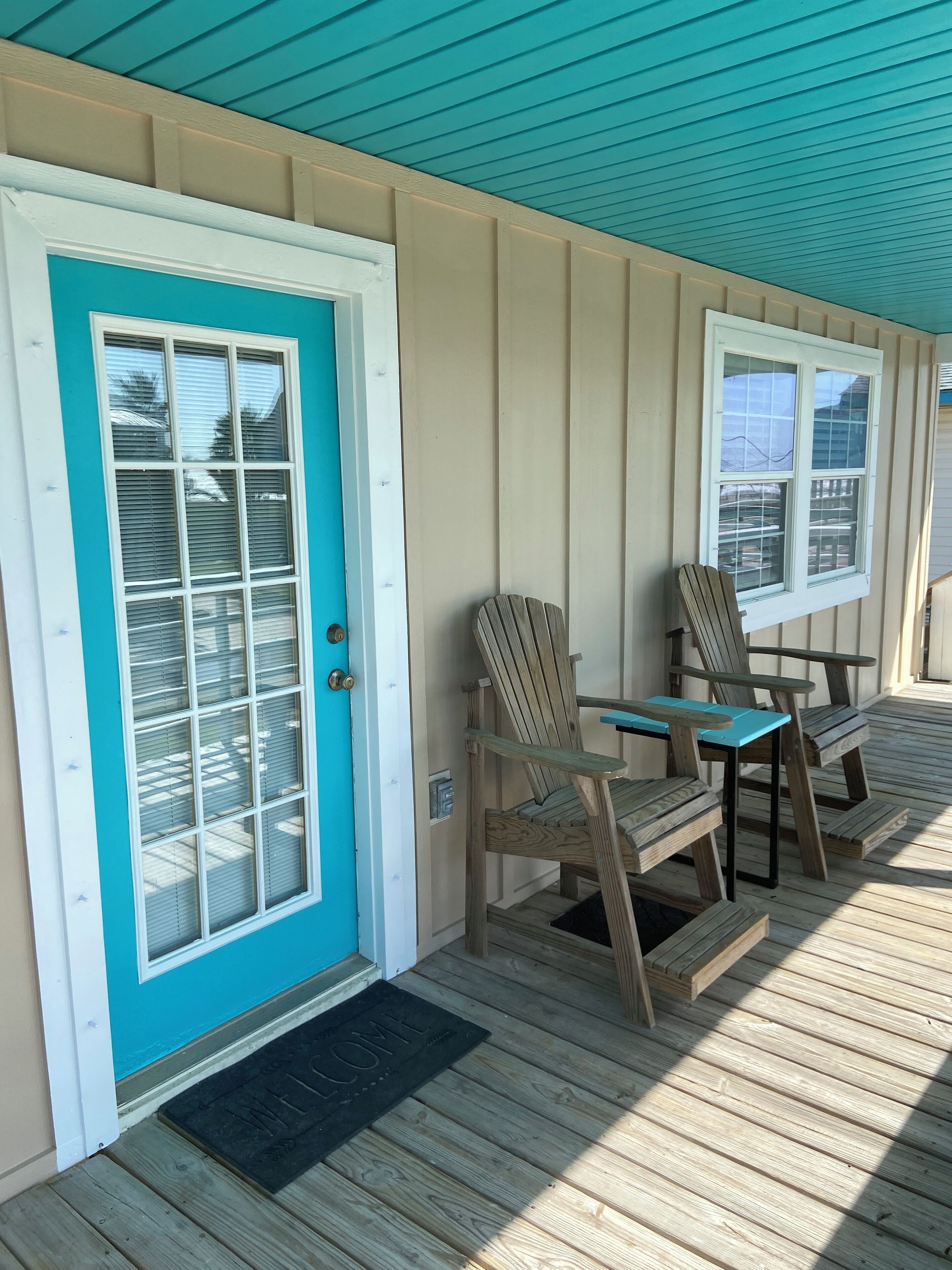 A wooden deck with a turquoise door and two wooden chairs.