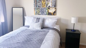 Un llit ben fet amb un sobrellit estampat, una taula de nit amb una làmpada, i una obra d'art penjada a la paret sobre el llit.