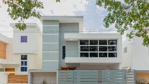 A modern two-story house with a light blue exterior, a large window on the second floor, and a gated driveway. - Mansión Versatil with a beautiful private pool 🏊‍♀️ 5 min from movies/groceries  (La Romana)