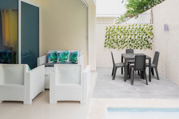 A patio area with a pool, white wicker furniture, and a table with chairs.