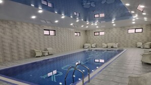 En stor indendørs swimmingpool med tydelige baneafmærkninger, omgivet af liggestole og flisegulv.