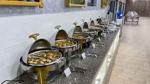 En buffetopsætning med flere rustfrie serveringsfade med forskelligt mad, arrangeret i en række langs en marmorvæg.